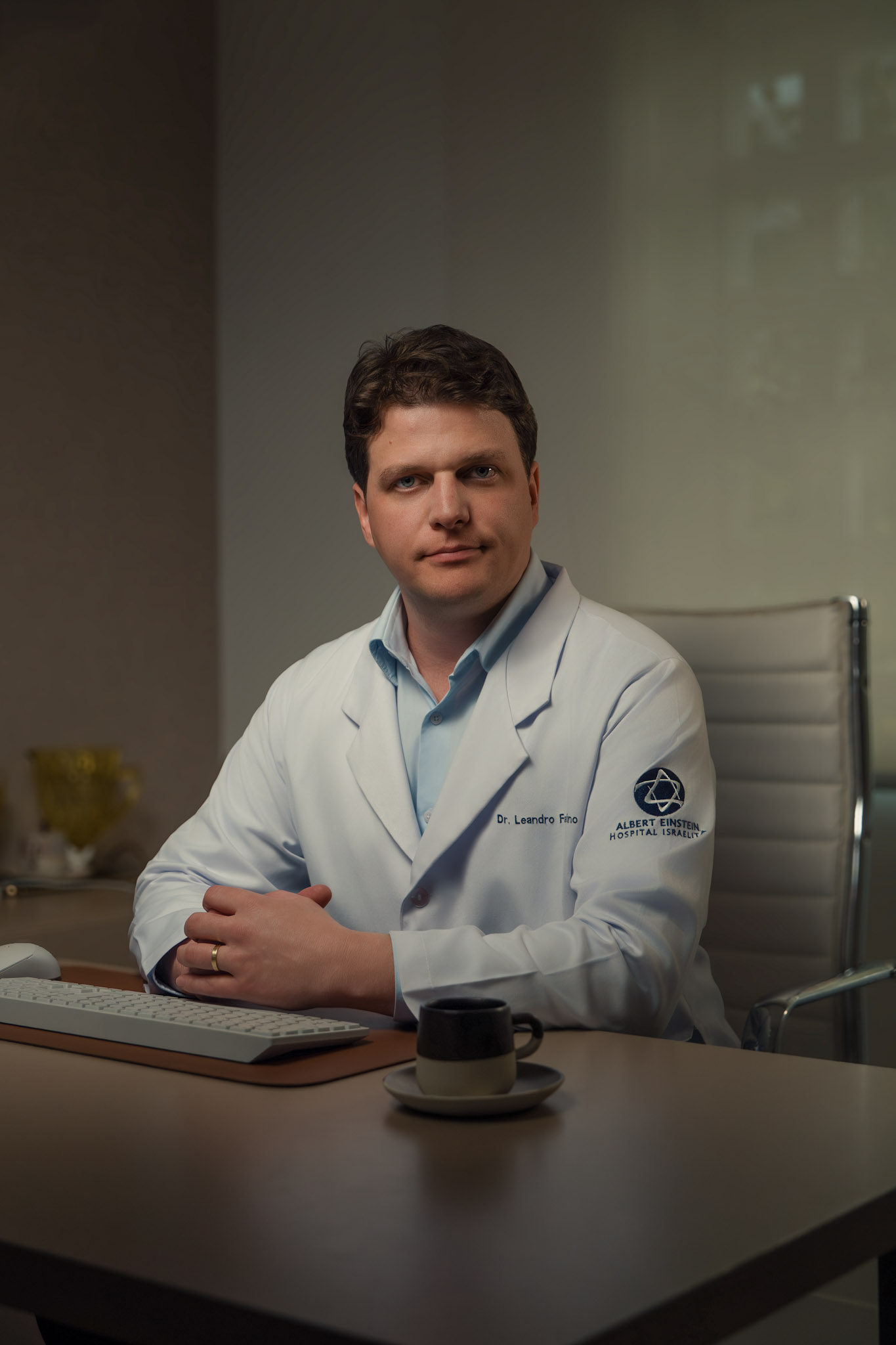 Dr. Leandro Faustino sentado à mesa do consultório, com jaleco