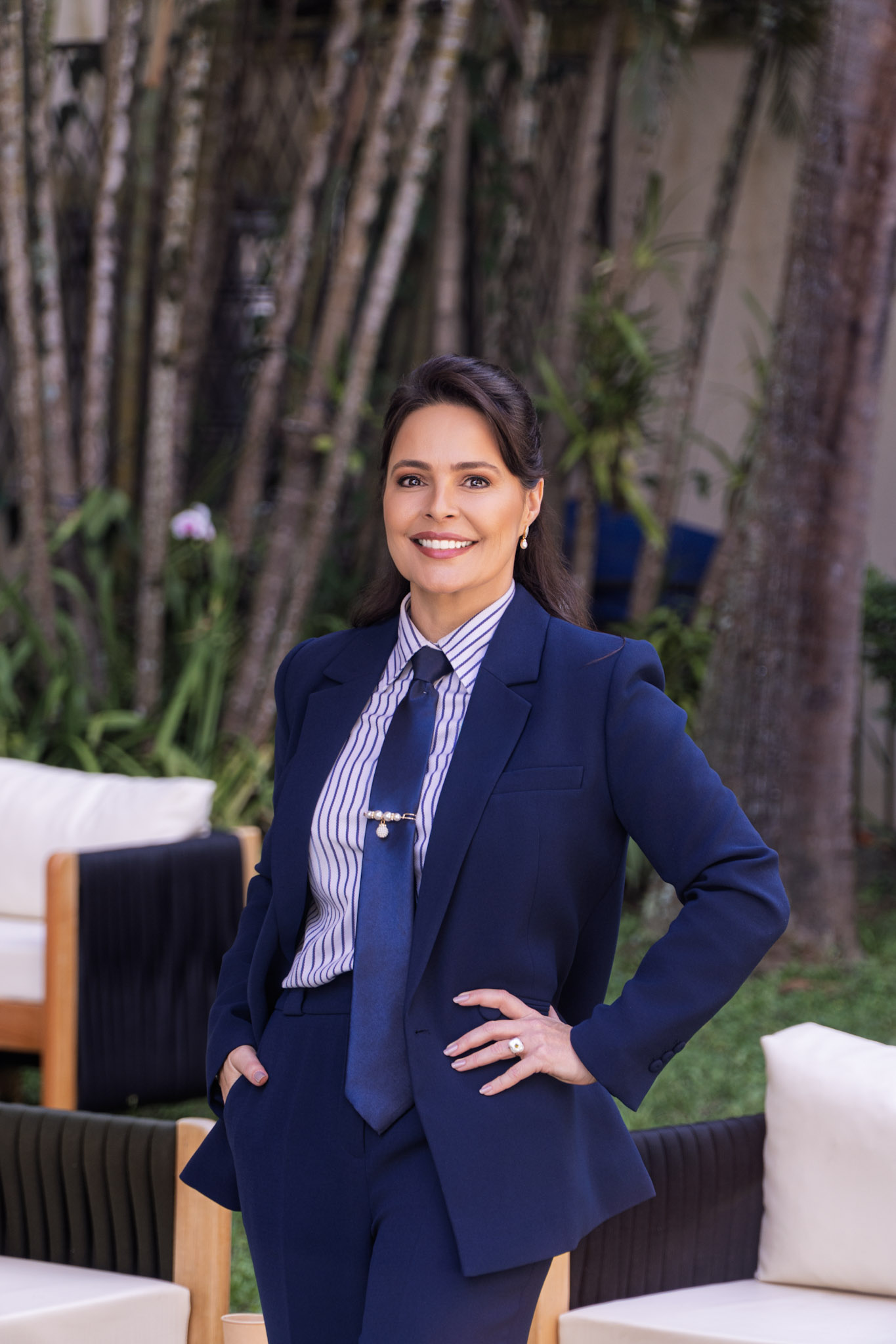Gabriella Florêncio em alfaiataria azul-marinho com gravata e a mão na cintura